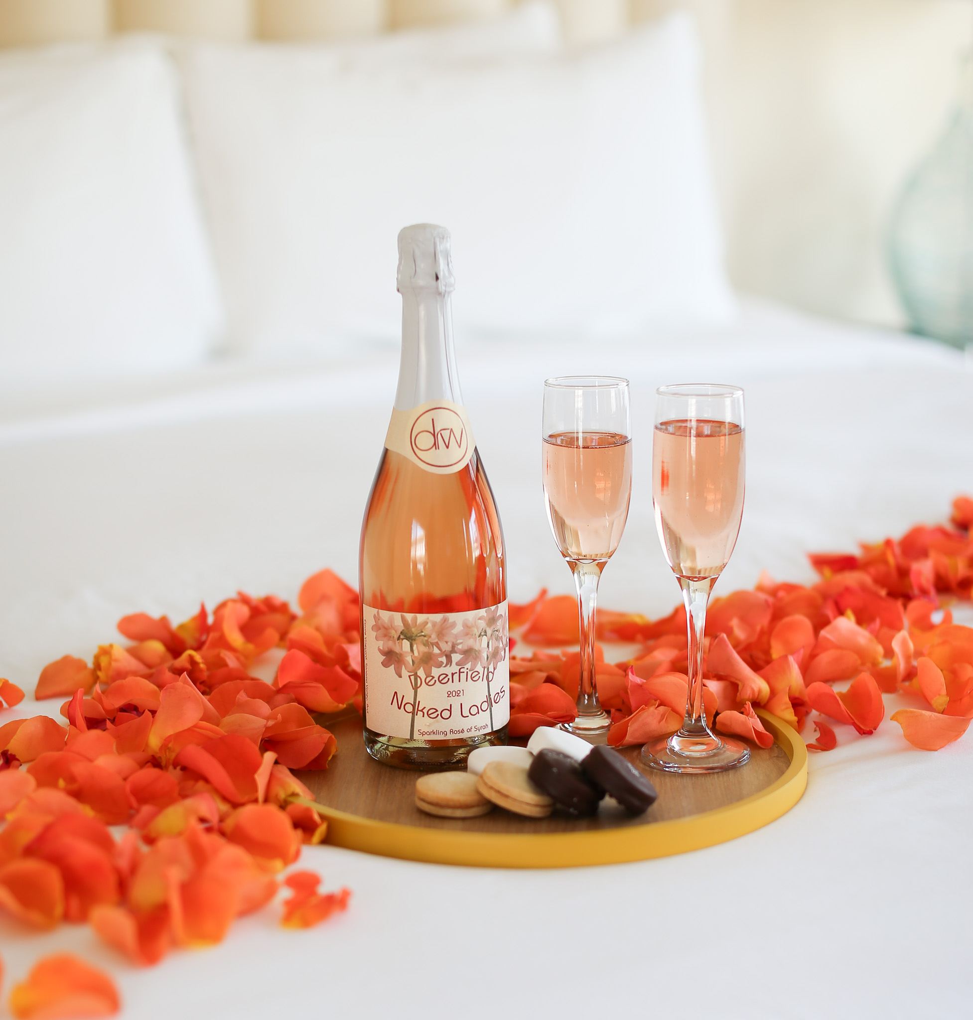 Champagne bottle beside two filled glasses on a gold tray with flower petals alongside